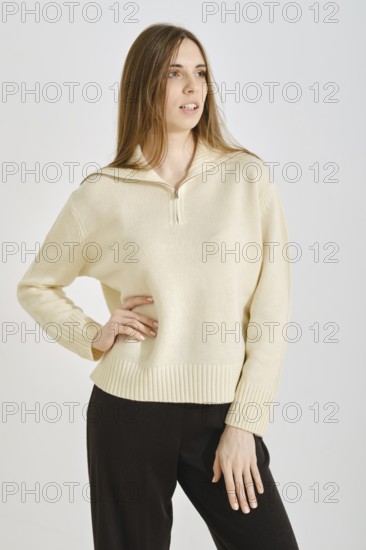 A woman showcases a stylish, cream-colored sweater paired with black trousers in a minimalist