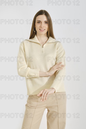 Cheerful woman in a light cream sweater and beige pants posing over white background. The outfit