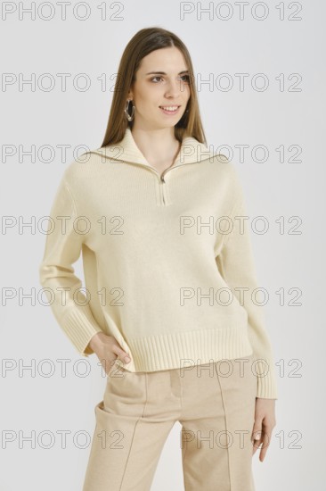 A young woman poses in a trendy cream sweater with a zip collar paired with beige pants. This