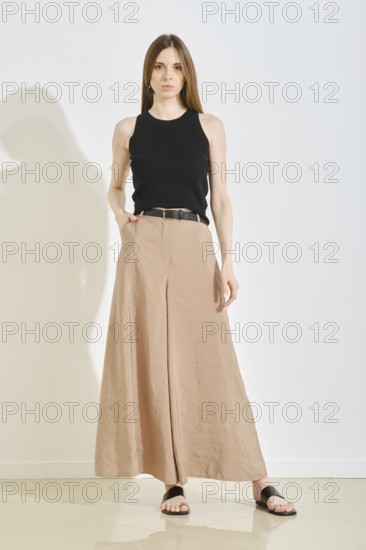 A young woman showcases a stylish outfit with a fitted black tank top and elegant beige wide-leg
