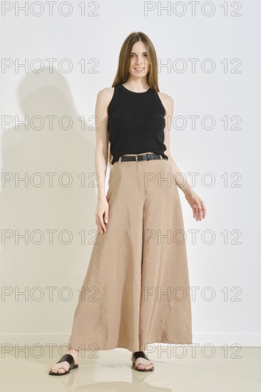A young woman stands confidently in a trendy outfit, showcasing wide-legged beige pants and a black