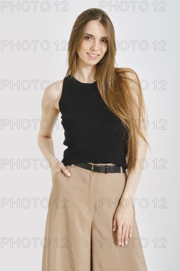 A woman stands confidently in a trendy female outfit, featuring a black tank top and beige wide-leg