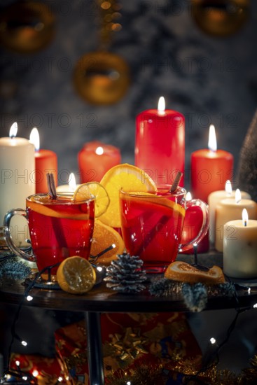 Two glasses of mulled wine with cinnamon and oranges in front of red and white candles, Christmas