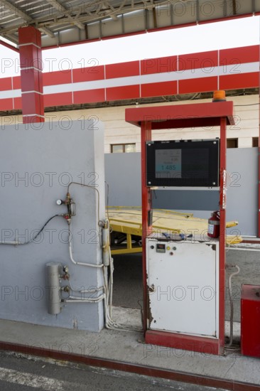Red gas pump with screen and cables in front of a grey wall, gas filling station, Sewan,