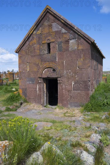 Old Armenian stone church with vaulted entrance surrounded by green landscape, Noratus cemetery,