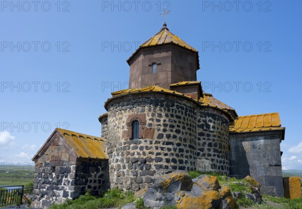 Historic stone church with a round tower in a rural setting under blue sky, Hajravank Monastery,