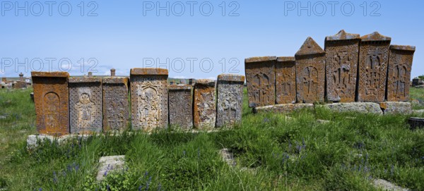 Series of engraved stone monuments on a sunny, green meadow, crossstones, khachkars, world's