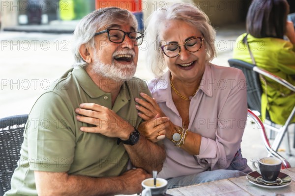 Mature couple laughing and chatting over coffee on a sunny outdoor cafe patio, enjoying relaxed