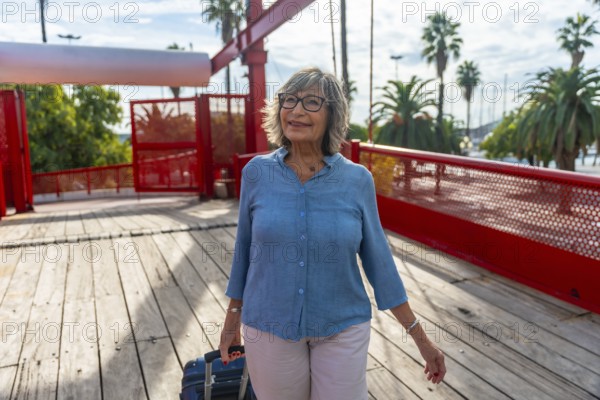 Senior woman walking across a pedestrian bridge with her luggage, enjoying an urban vacation on a