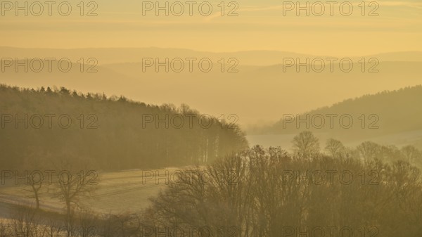 Blurred hills and golden sky at sunrise create a misty, quiet landscape, Seckmauern, Lützelbach,