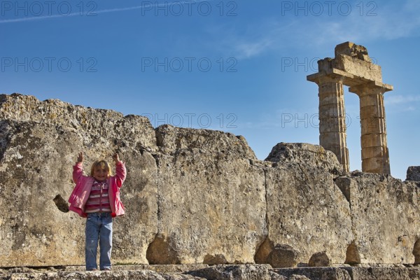 Child standing in front of an ancient column. Stones and sky in the background, Nemea, Ancient Zeus