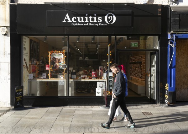 Shoppers passing Acuitis opticians and hearing centre shop store, High Street, Exeter, Devon,