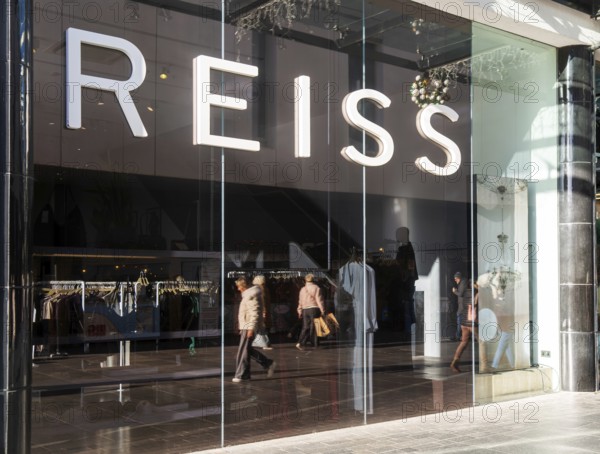 Shoppers walking reflected in Reiss shop store window in city centre, Princesshay, Exeter, Devon,