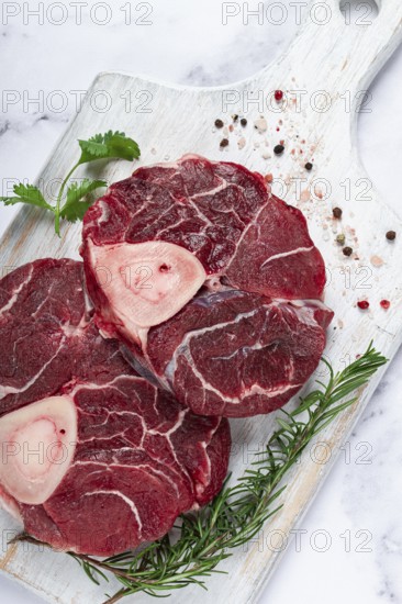 Knuckle on the bone, raw meat for ossobuco, on a wooden chopping board, with a sprig of rosemary,