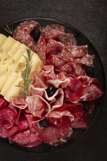 Cold cuts, appetizer, prosciutto, salami and ham, with maasdam cheese and olives, on a round plate,