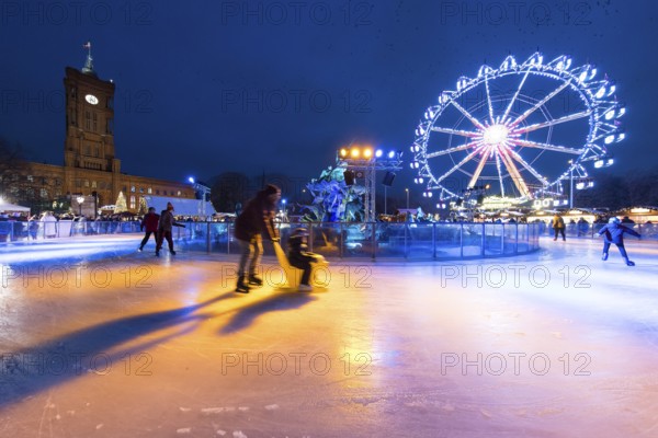 Skaters in front of the Red Town Hall, Neptune Fountain and a Ferris wheel at the Berlin Christmas