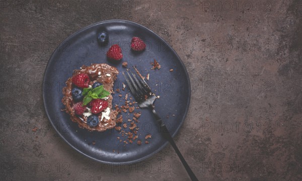 Half-eaten chocolate tartlet, on a plate, stuffed with cottage cheese and berries, breakfast,
