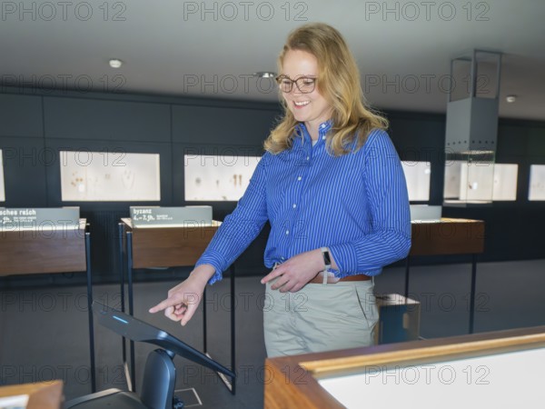 A woman in a blue shirt smiles and uses a digital screen in a museum, robotic personality
