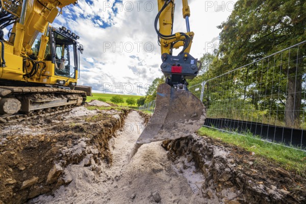 An excavator lifts soil from a deep ditch on a construction site in cloudy skies, construction PV