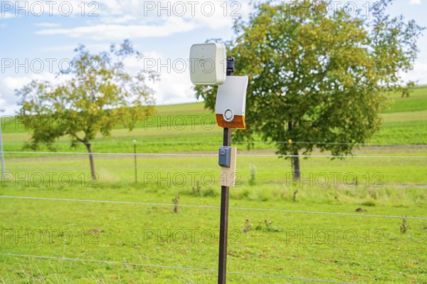 Camera on a post, surrounded by green fields and trees, against a cloudy sky, Bau PV