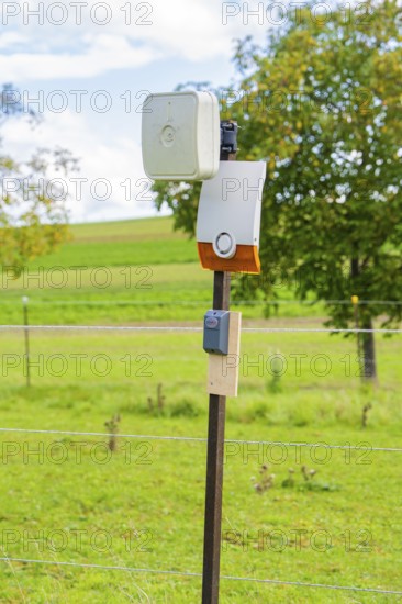 Camera mounted on a fence post in a rural landscape in front of a green field, Bau PV