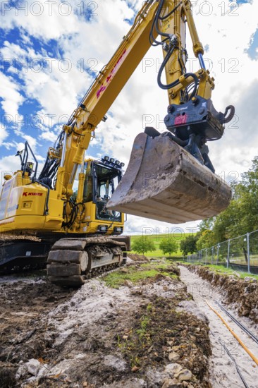 Large excavator digging a trench under cloudy sky, Bau PV Freifaechenanlage, Weil der Stadt,