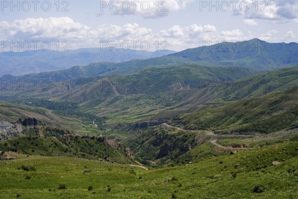 Rolling hills and mountains around a wide valley with green vegetation, cloudy sky, views from