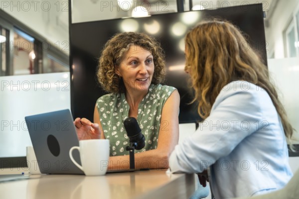 Two professional women collaborating on a podcast, recording a conversation with a microphone and