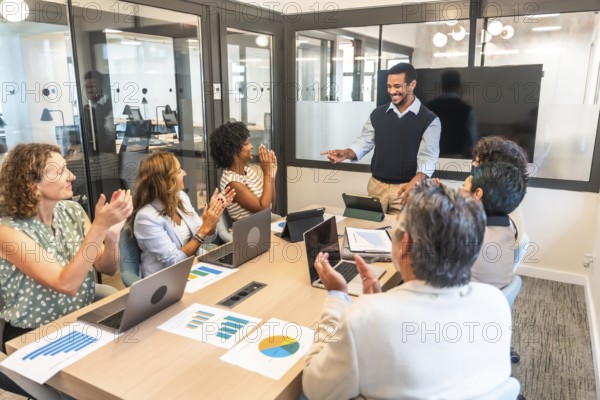 Diverse business team in a modern boardroom applauding a smiling presenter, celebrating project