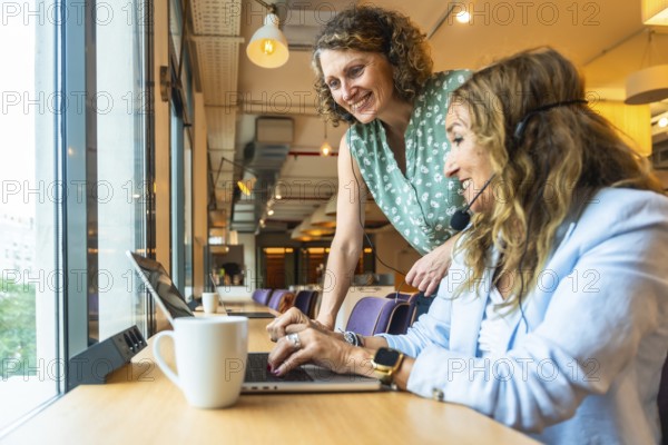 Two smiling women are collaborating and supporting each other while wearing headsets, working on