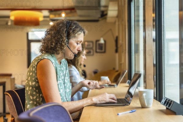 Women concentrating on their work using laptops and headsets in a modern coworking office,