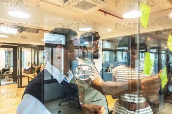 Business colleagues collaborating on a project, writing ideas on sticky notes affixed to a glass