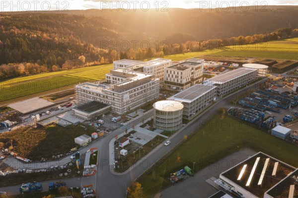 Modern buildings surrounded by fields and hills at sunset, aerial view, new hospital, Calw health