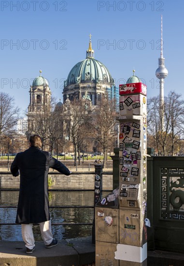 A man stands next to a demolished modern Telekom telephone column, view of Lustgarten Cathedral,