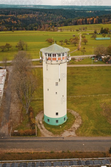 White water tower in rural autumn landscape with green fields and autumnal trees, water tower,