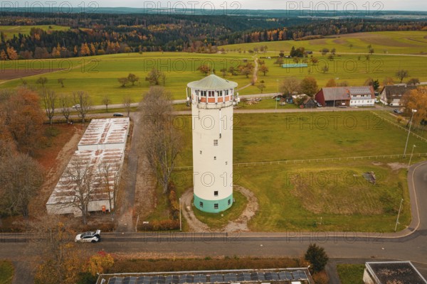 Water tower in the middle of a vast landscape with fields and small buildings in the background,