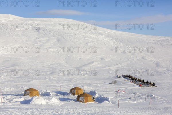 Snowmobiles, snow scooters at Arctic expedition camp with tents protected by tripwire fence against