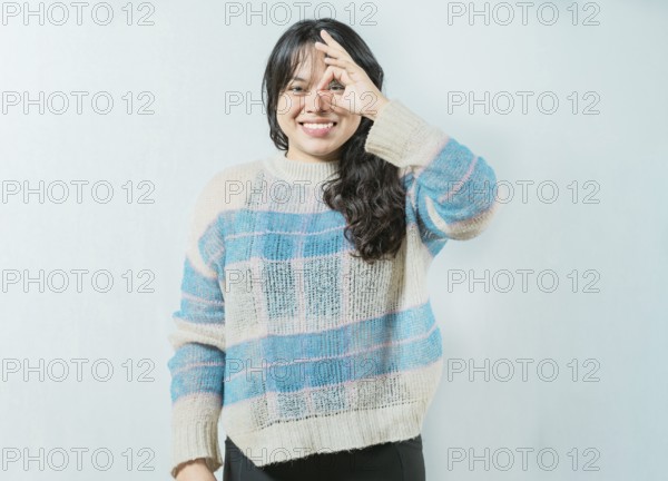Beautiful asian woman making OK gesture looking through fingers isolated. Smiling asian girl making
