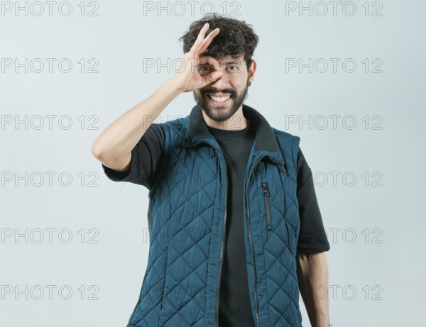 Cheerful guy making ok gesture looking through fingers. Handsome young man making OK gesture