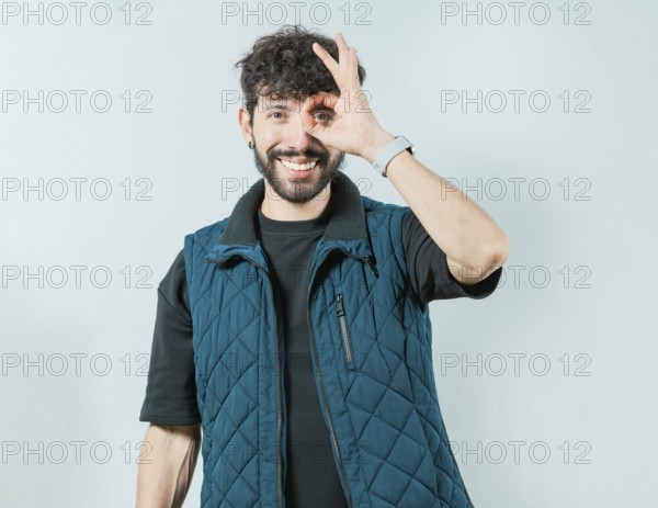Handsome young man making OK gesture looking through fingers isolated. Cheerful guy making ok