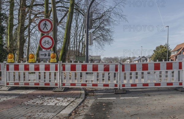 Road block with warning signs and yellow lights surrounded by bare trees in winter, Münsterland,