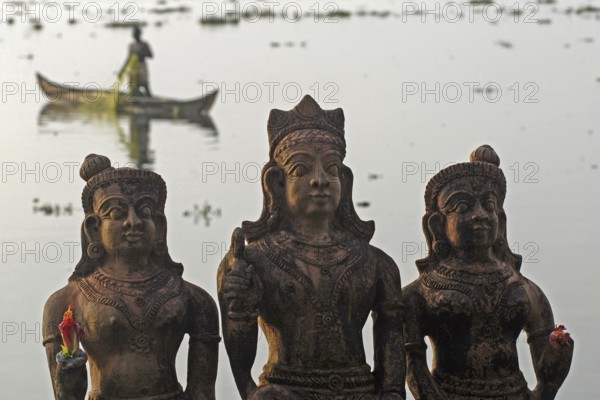 Three Hindu god statues made of clay, fishermen in a boat in the background, Vembanad Lake, Kerala,