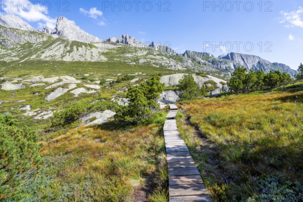 Wooden plank trail through mountain moor, in front of picturesque mountain landscape, Göscheneralp,