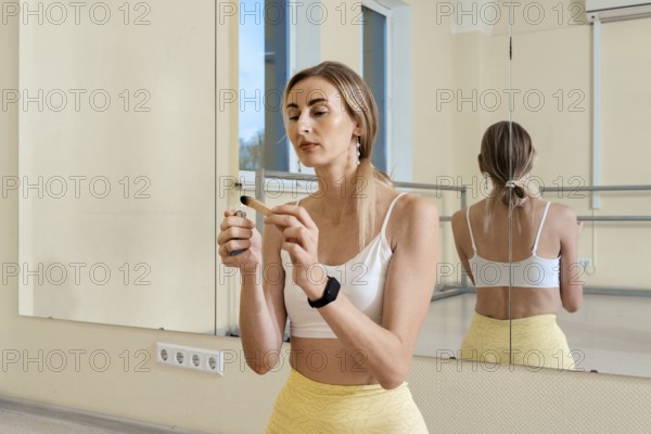 In a bright studio, a woman wearing a white top and yellow pants ignites palo santo the incense