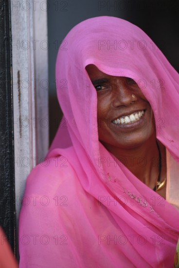 Smiling woman, face partly covered by long, scarf-like pink shawl or Dupatta, also known as Chunni,