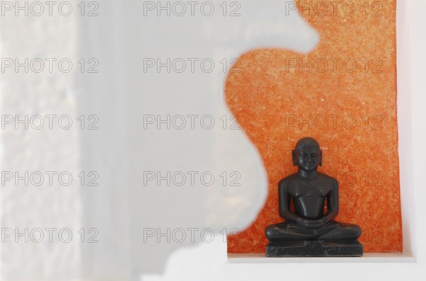 Statue of a black Buddha sitting meditating against an orange background, Devigarh Palace Hotel,