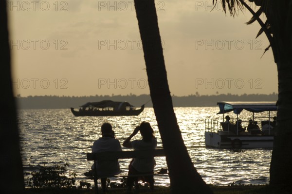 A couple sitting on a lakeside bench at sunset, boats gliding in the water, romantic atmosphere,
