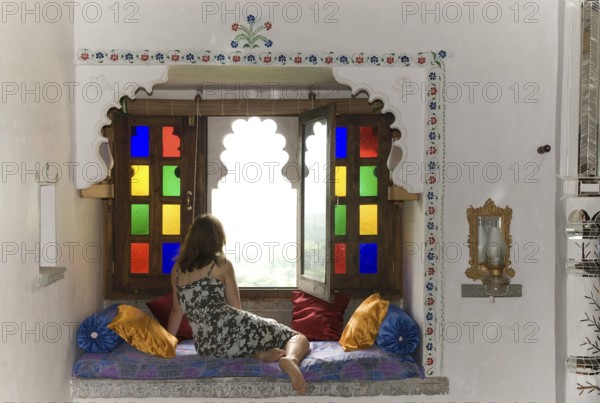 Woman wearing a dress in a cozy sitting area with pillows in front of colorful window, Palasthotel