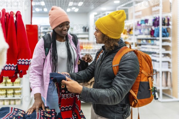 Young diverse couple choosing festive holiday ugly christmas sweaters in a retail store, enjoying