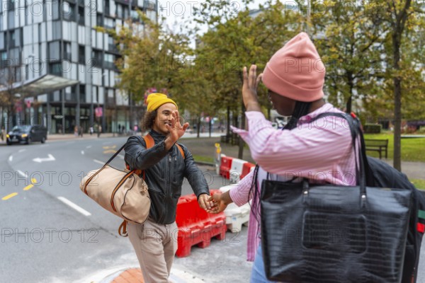Young diverse couple extending hands for a high five, holding hands, and carrying bags while